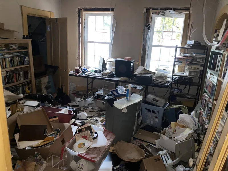 Room cluttered with papers, electronics, and debris